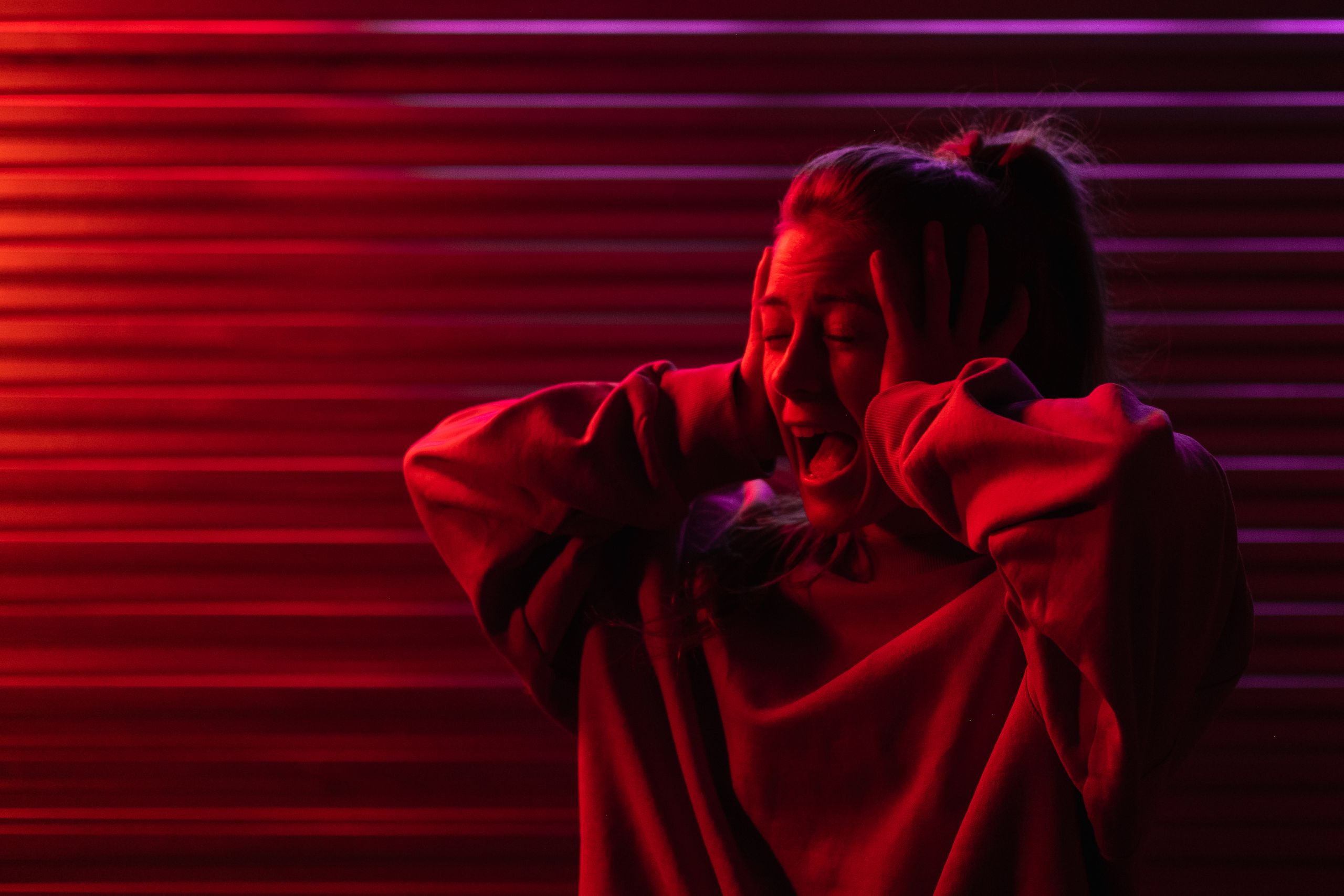 Crying frustrated woman with eyes closed in hoodie in bright ultraviolet light in darkness